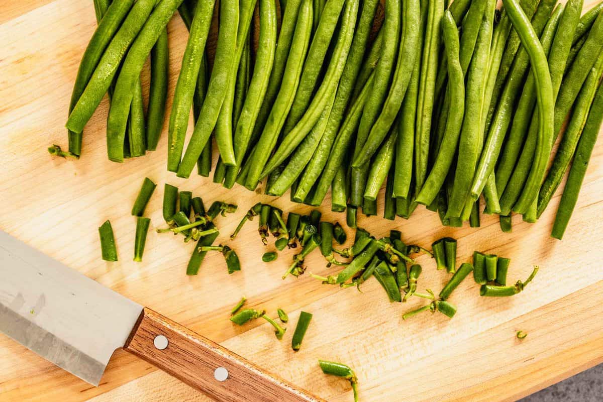 trimmed green beans on a wood cutting board with a knife