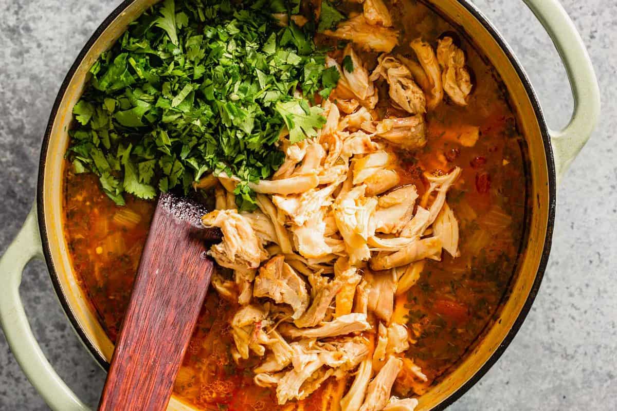 shredded chicken and cilantro on top of a tomato broth in a large pot