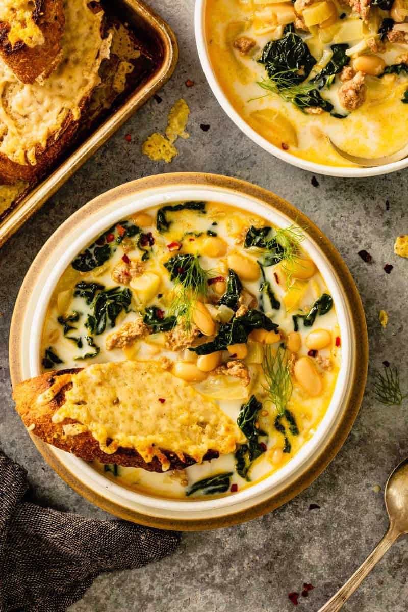 creamy soup in a shallow white bowl with white beans, kale and sausage and a cheesy toast set in the soup