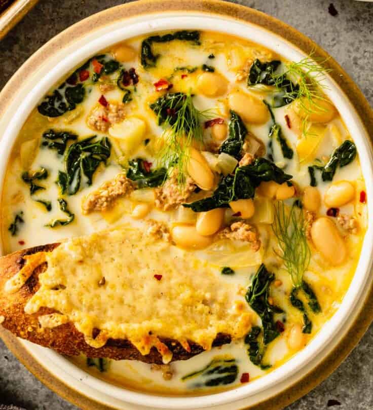 creamy soup in a shallow white bowl with white beans, kale and sausage and a cheesy toast set in the soup