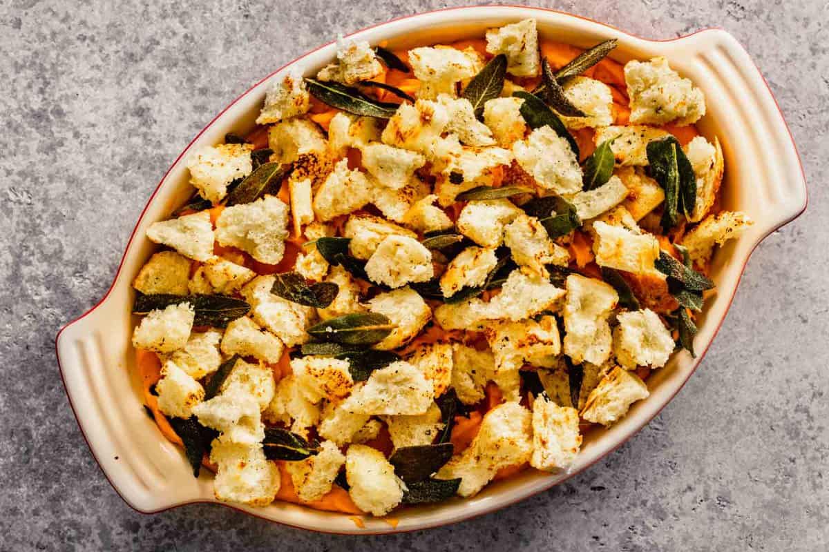 casserole dish filled with sweet potato filling and topped with croutons and sage