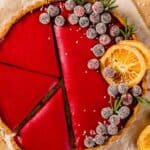 golden brown tart crust filled with a vibrant red filling and topped with candied cranberries, rosemary, and candied oranges