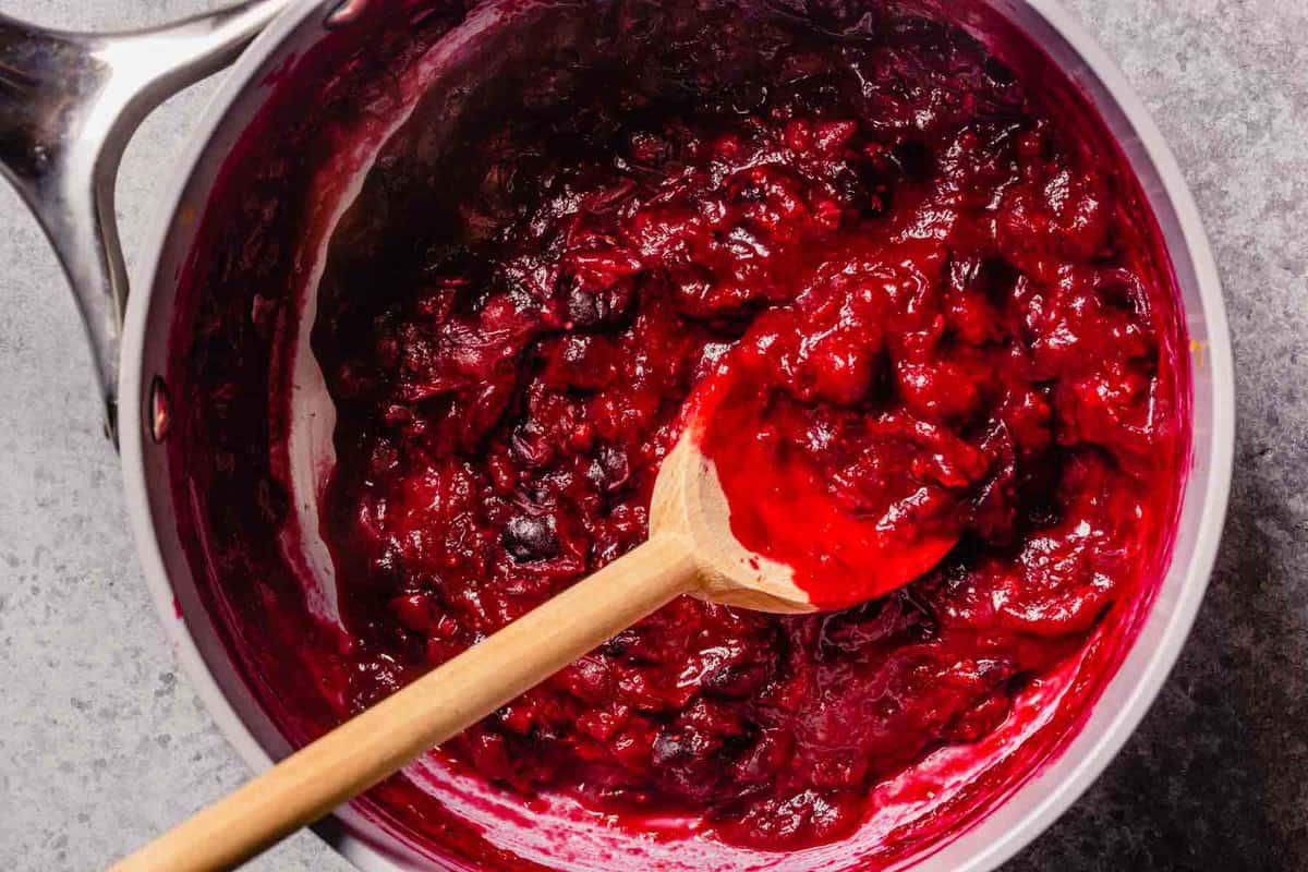 cooked cranberry mixture in a gray saucepan with a wooden spoon.