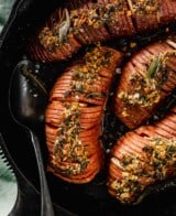 hasselback sweet potatoes topped with an herby garlic mixture in a cast-iron skillet