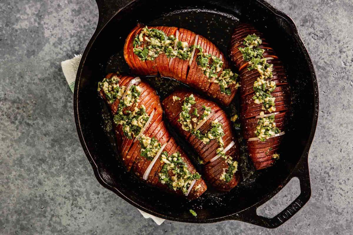 hasselback sweet potatoes topped with an herby garlic mixture in a cast-iron skillet