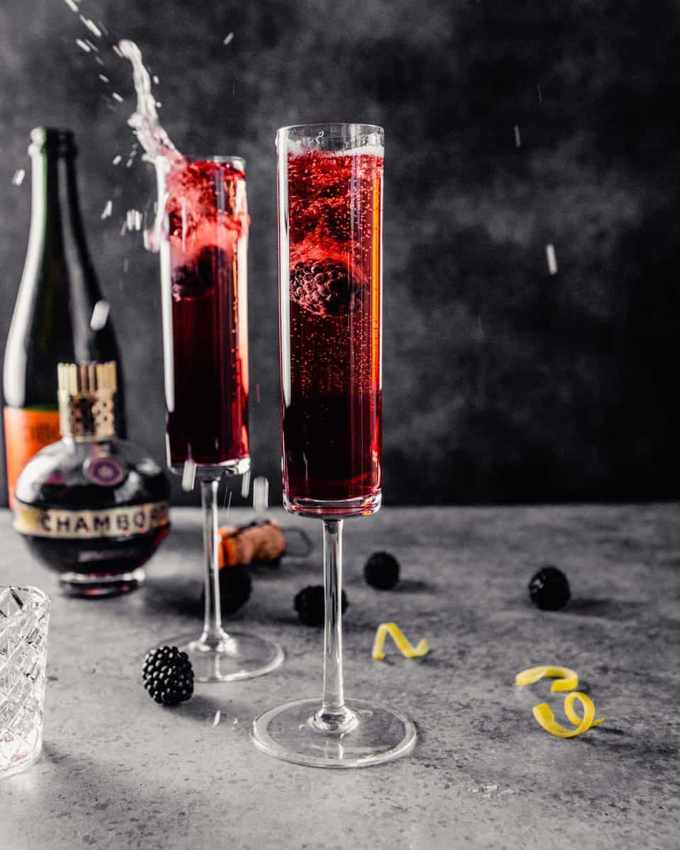 purple champagne cocktail in champagne flutes, garnished with a blackberry and lemon twist