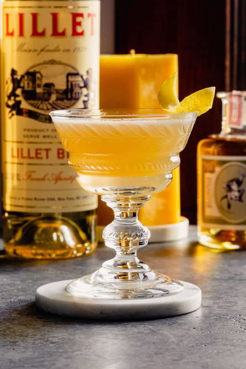 yellow cocktail in a coupe glass set on a white coaster