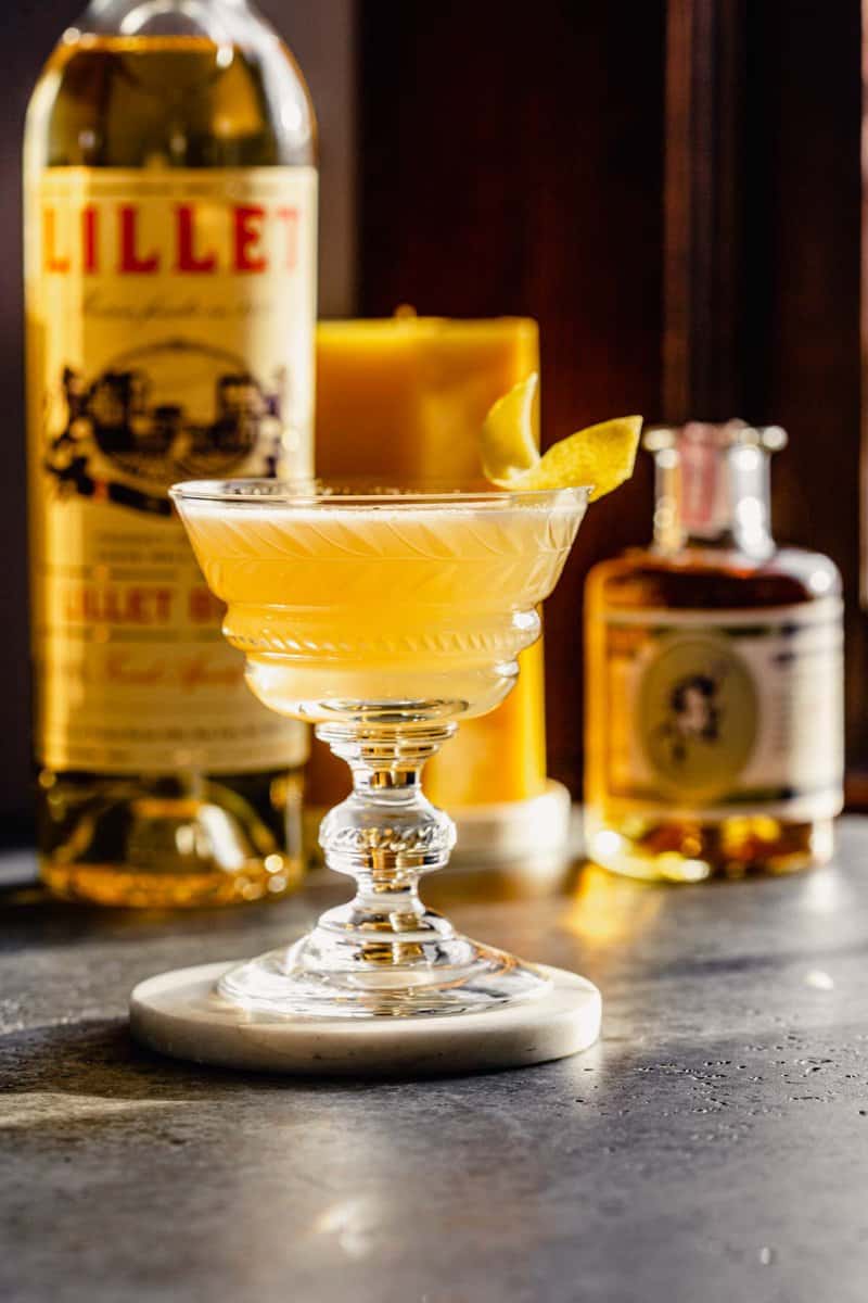 yellow cocktail in a coupe glass set on a white coaster