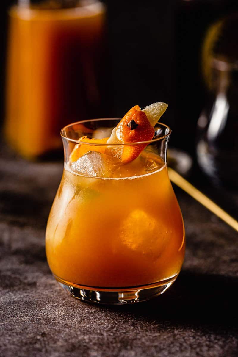 orange-colored cocktail in a rocks glass garnished with ginger and orange