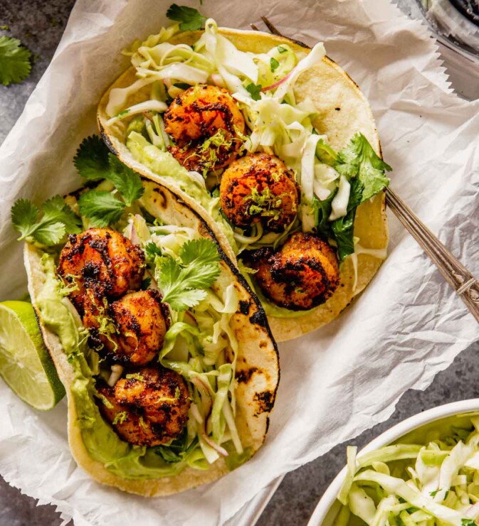 spiced shrimp in tortillas with slaw and avocado spread. tacos set in small parchment-lined baking sheets