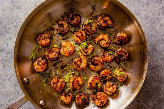 cooked shrimp in a skillet with lime zest over top