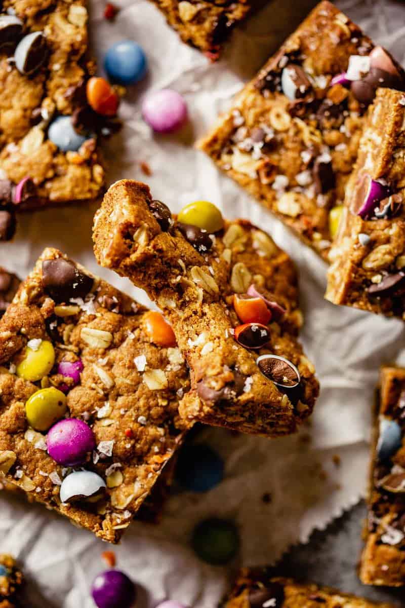 cookie bars made with chocolate chips, oats and m&ms set on crumpled parchment paper