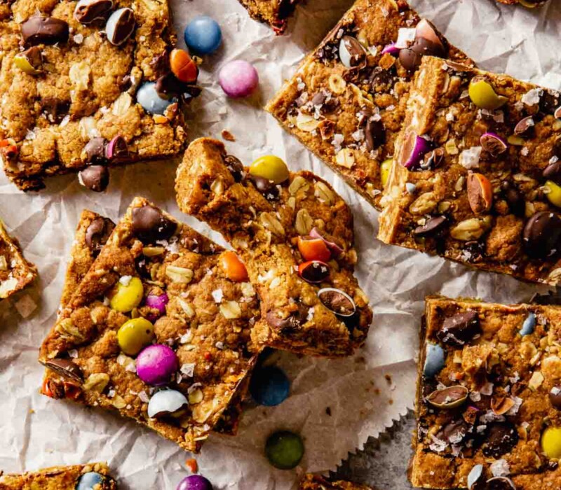 cookie bars made with chocolate chips, oats and m&ms set on crumpled parchment paper