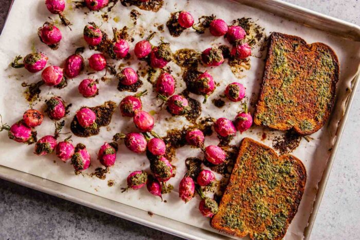 butter and herb-topped roasted radishes and bread on a baking sheet