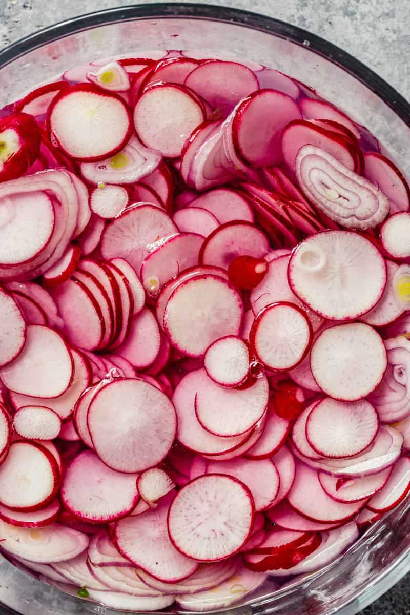 thinly sliced radishes and shallot in a clear glass bowl filled with water