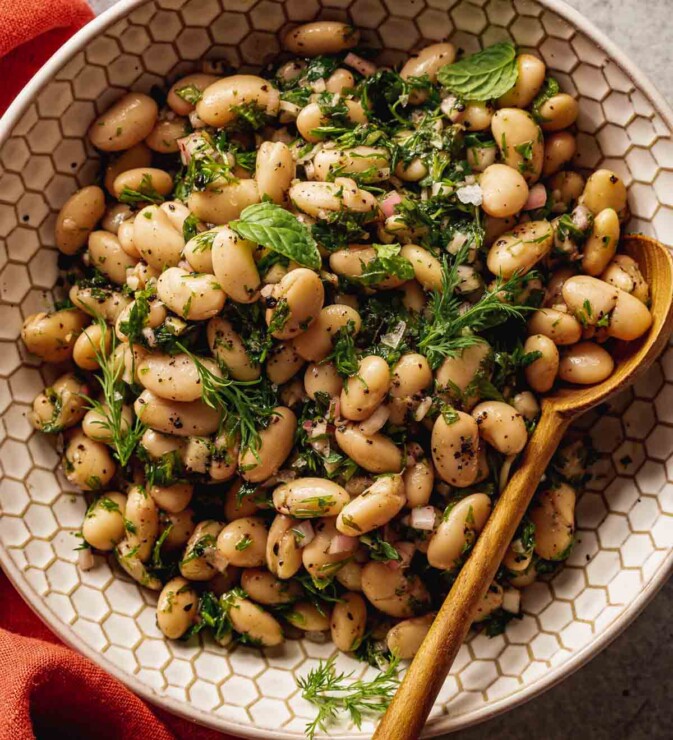 white beans and herbs in a white-textured bowl with a wooden spoon