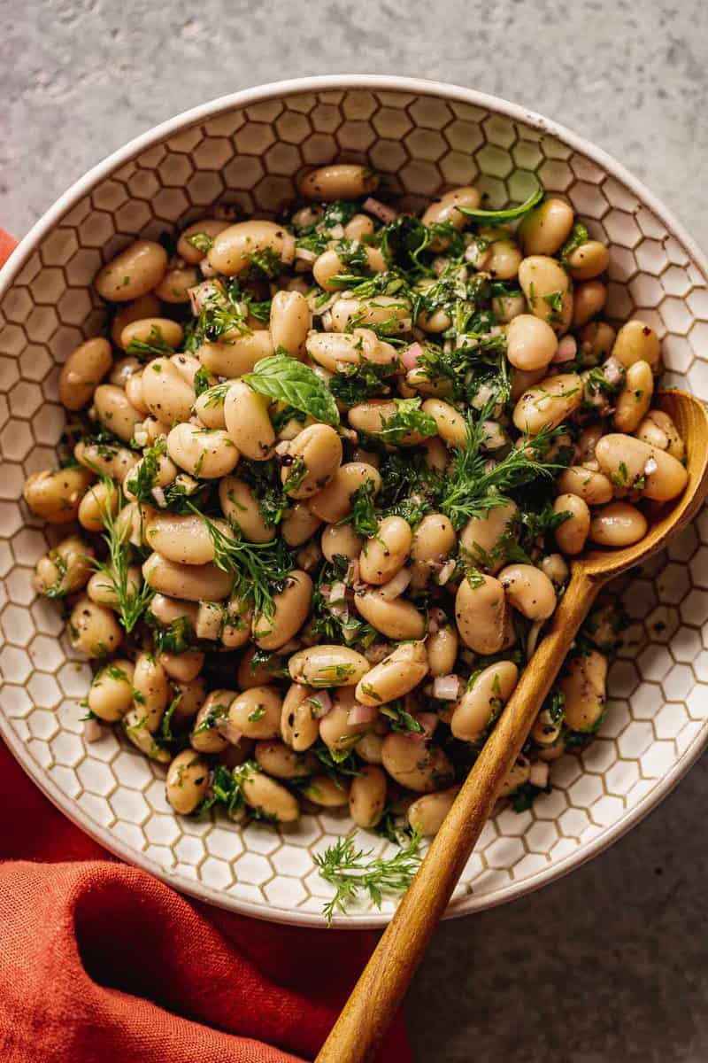 white beans and herbs in a white-textured bowl with a wooden spoon