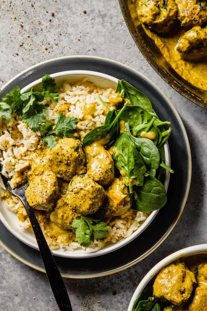 meatballs and a creamy curry sauce served over rice and topped with cilantro in a shallow white bowl