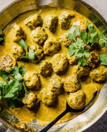 a pan filled with meatballs and a curry sauce topped with cilantro