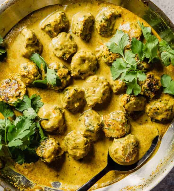 a pan filled with meatballs and a curry sauce topped with cilantro