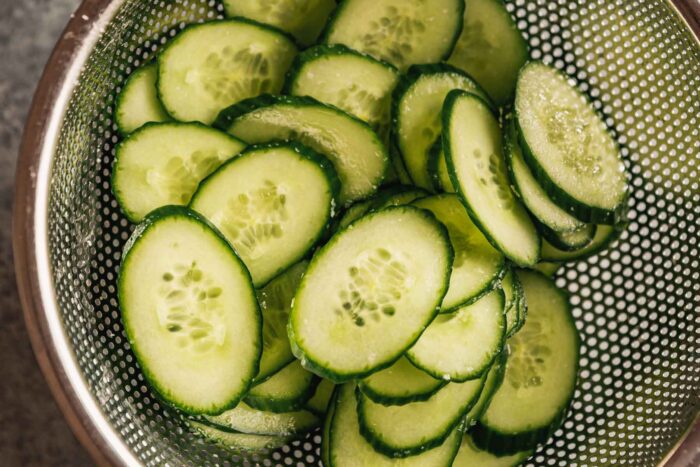 thinly sliced cucumber in a colander