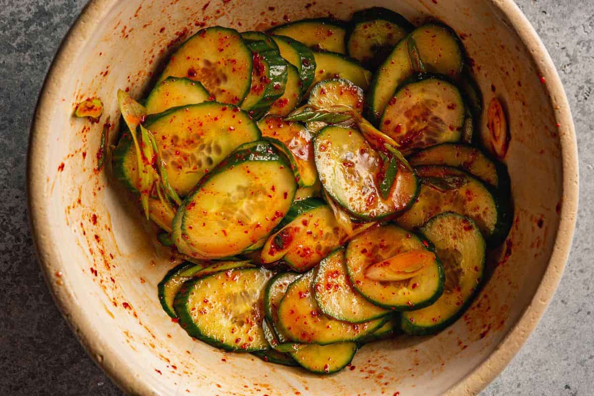 cucumber sliced coated in a red chili dressing in a brown bowl