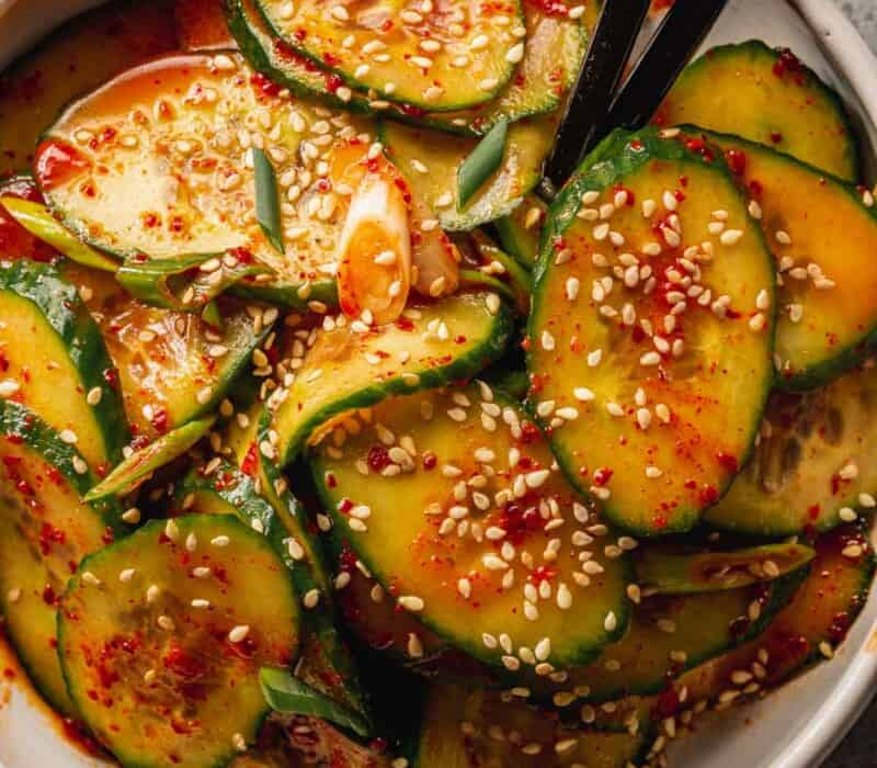 cucumber sliced coated in a red chili dressing in a white bowl with black chopsticks