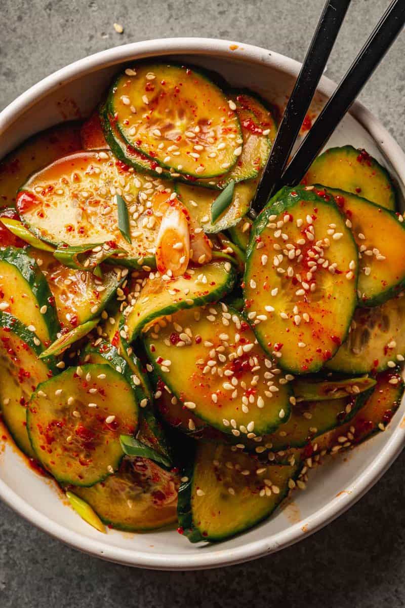 cucumber sliced coated in a red chili dressing in a white bowl with black chopsticks