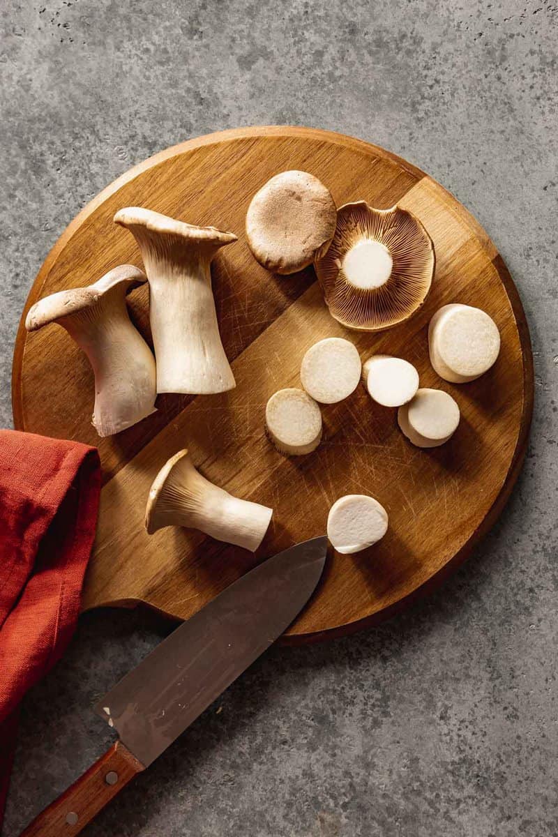 trumpet mushrooms on a wood cutting board with a chefs knife resting nearby