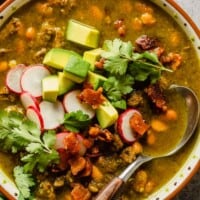 beef and bean stew in a multi-colored bowl topped with avocado, cilantro, radish and bacon bits