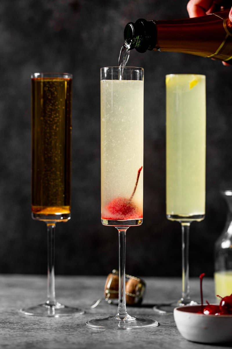 three champagne flutes on a counter one lightly orange hued, another slightly pink and the third yellow with a lemon peel