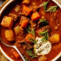 beef stew with potatoes in a red sauce and topped with sour cream and dill