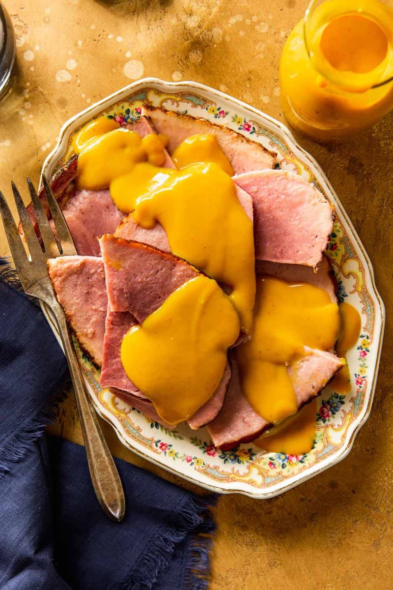 yellow mustard sauce drizzled over slices of ham on an ornate platter