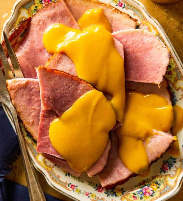 yellow mustard sauce drizzled over slices of ham on an ornate platter