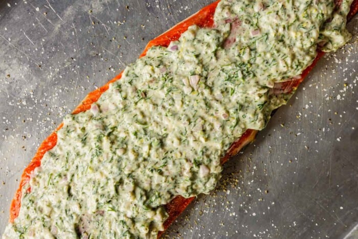 a large filet of salmon topped with herby mayo on a baking sheet