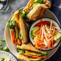 large white bowl with three large sandwiches and a bowl of pickled vegetables set in it