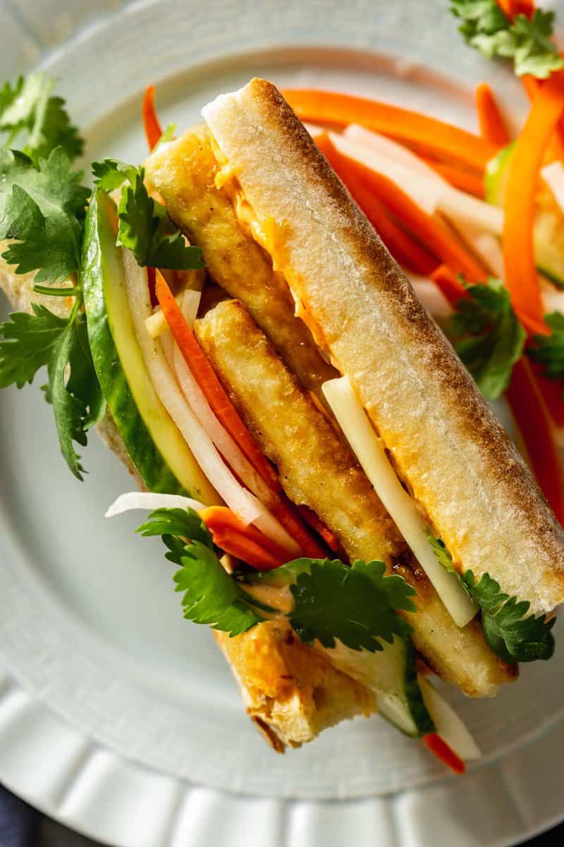 side view cut of a sandwich made with baguette, tofu slices, and vegetables