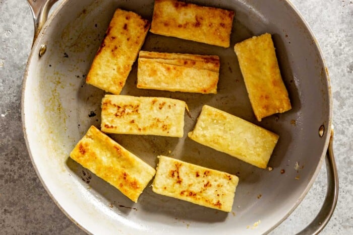 slices of fried tofu in a large gray skillet
