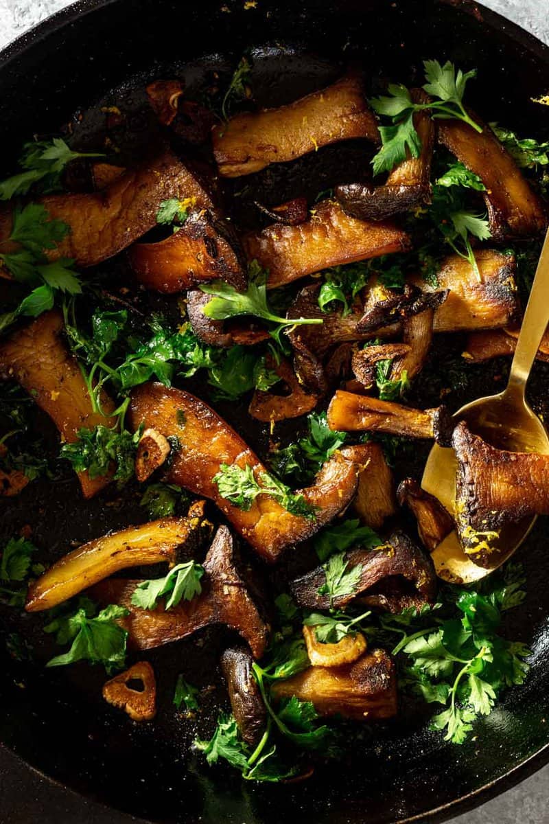 slices of king oyster mushrooms in a cast-iron skillet with parsley and lemon zest