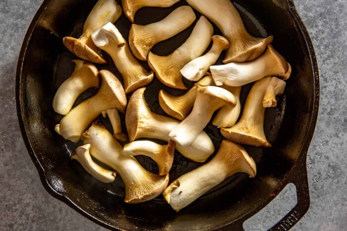 slices of king oyster mushrooms frying in a cast-iron skillet