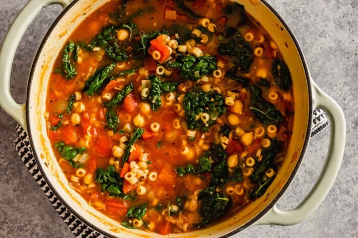 a soup make with kale, pasta and tomatoes in a large pot