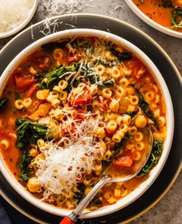 tomato soup with pasta, chickpeas and kale in a shallow white bowl set on a blue plate