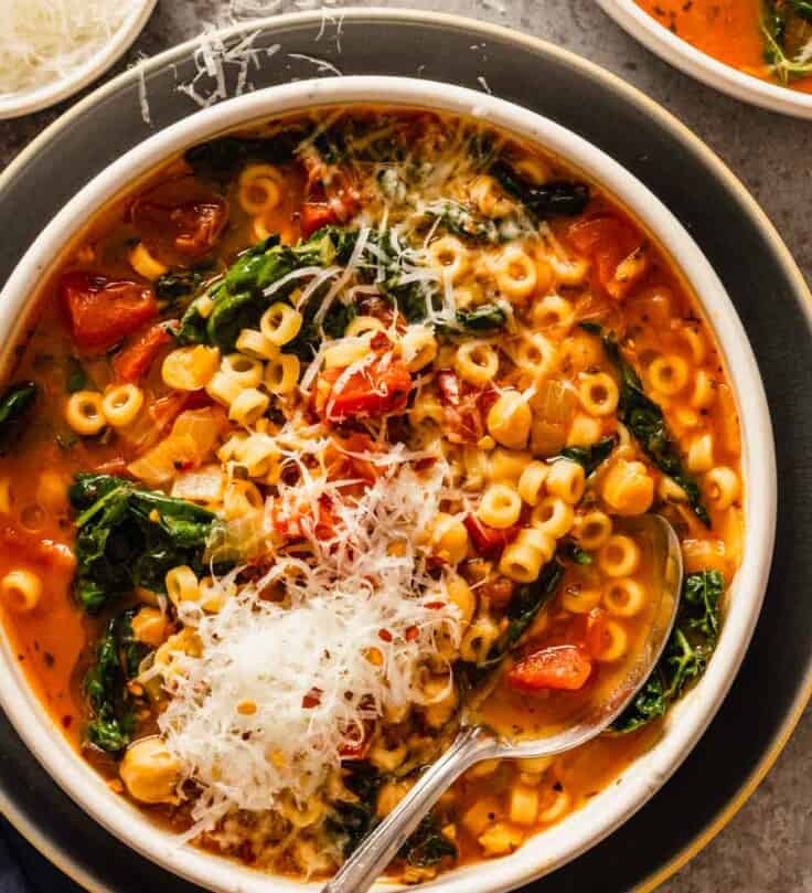 tomato soup with pasta, chickpeas and kale in a shallow white bowl set on a blue plate