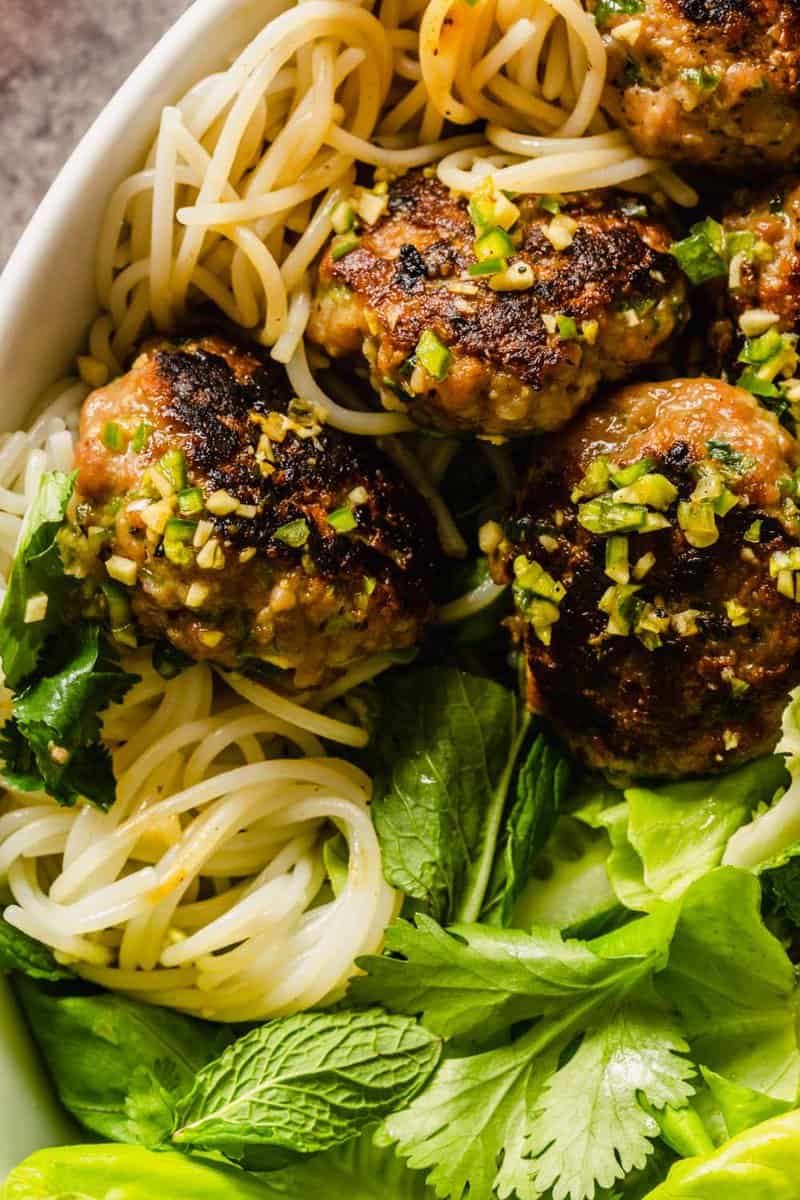 pork patties with minced garlic and serrano on top of them set on rice noodles