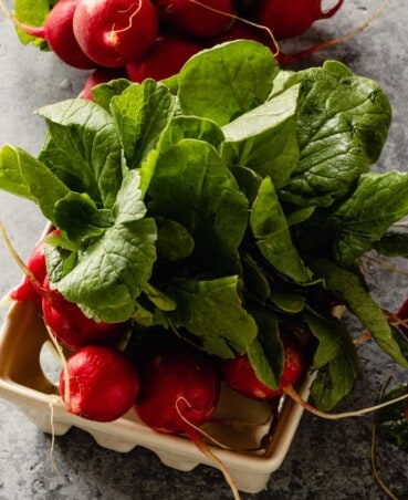 radishes with greens in a colander on a counter