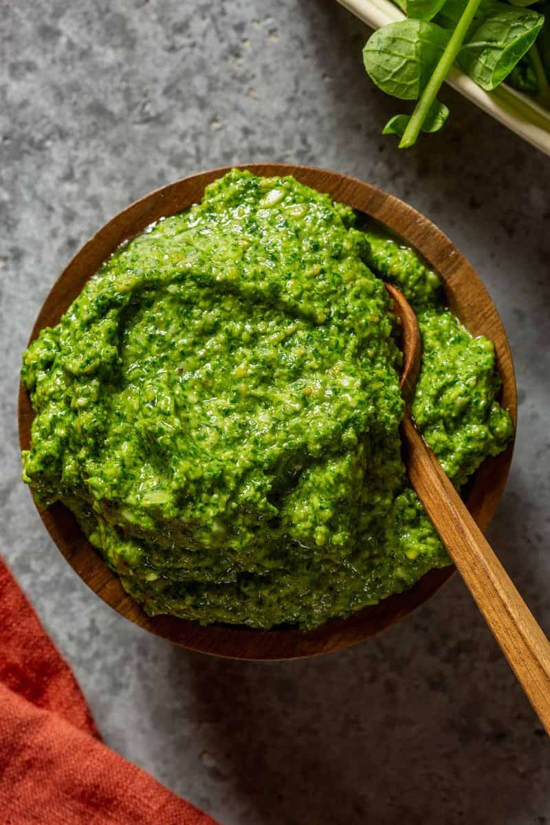 bright green pesto in a small wooden bowl with a small wood spoon set in it