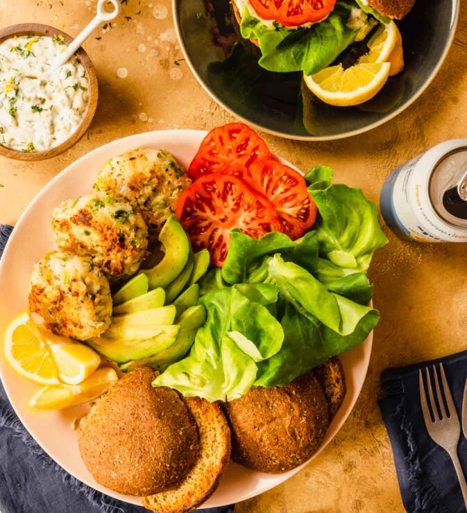shrimp burgers, lettuce leaves, tomato slices, avocado slices, toasted buns, and lemon slices arranges on a large platter