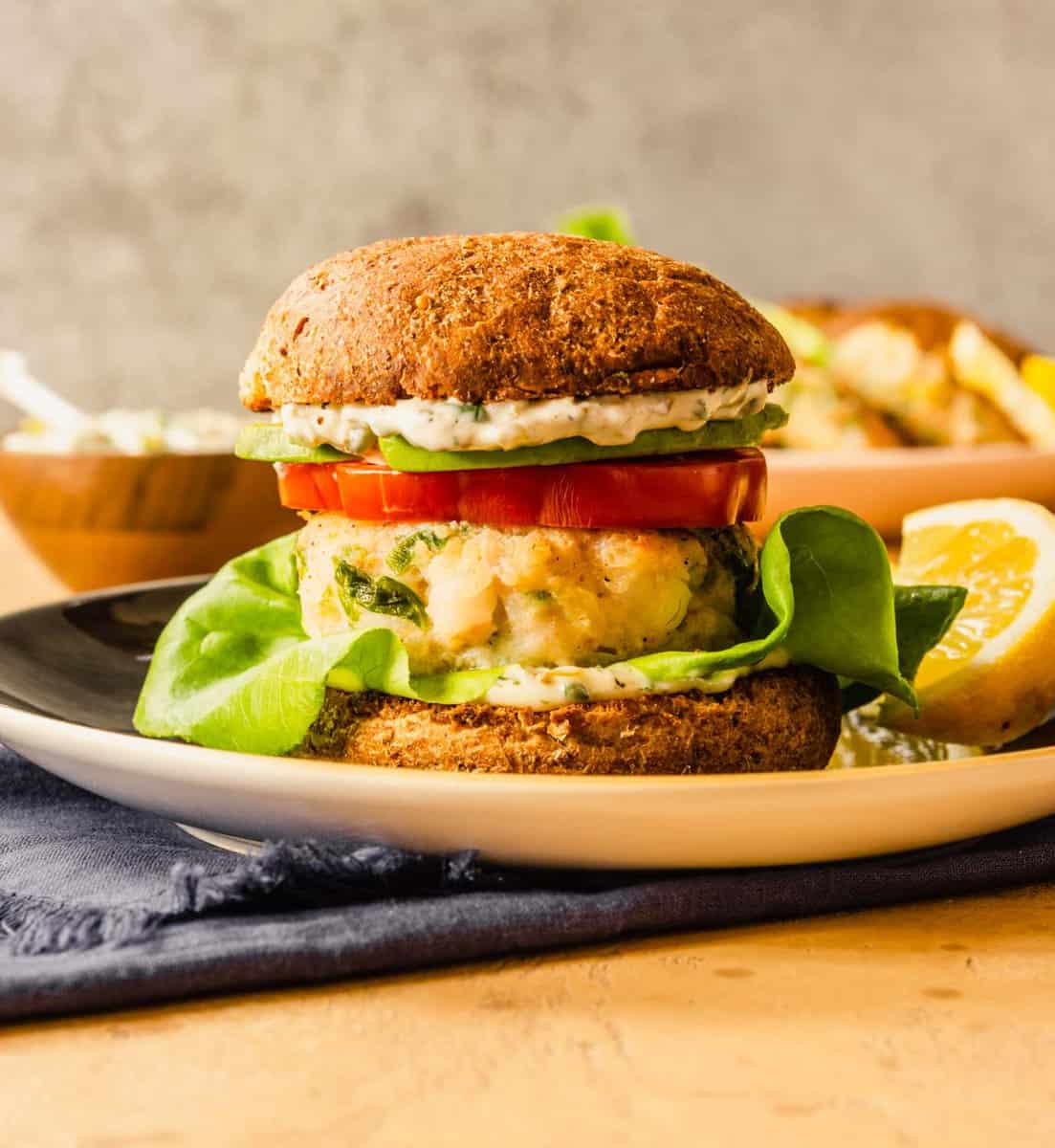 shrimp burger on a whole-wheat bun layered with lettuce leaves, a tomato slice, sauce and avocado slices