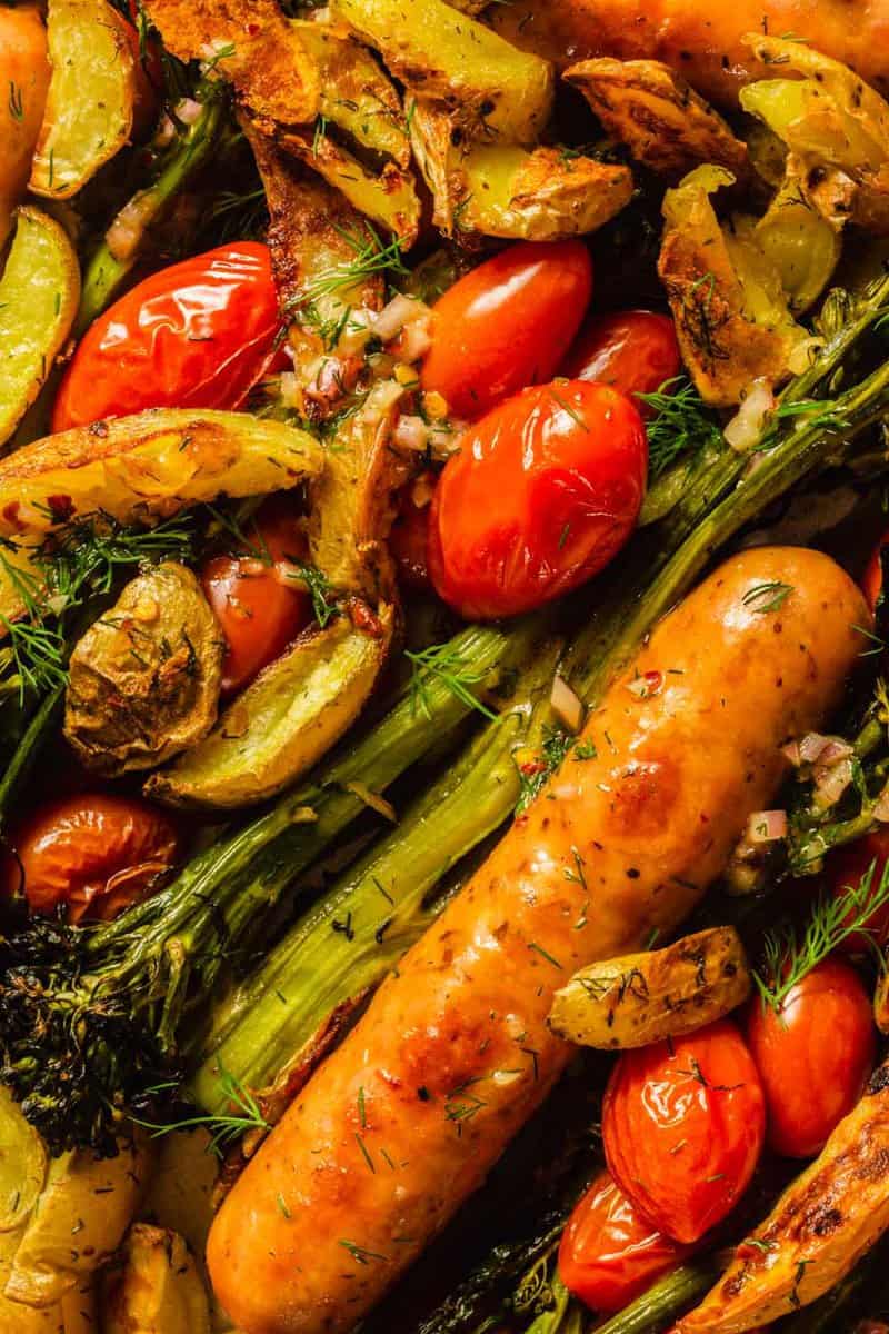 sausages, potato wedges, cherry tomatoes and broccolini on a baking sheet