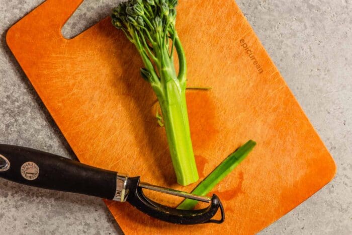 broccolini on a wood cutting board with a vegetable peeler